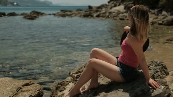 Jonge dame zit op de kustlijn op een zomerdag. - Video