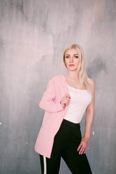 Attractive positive middle-aged blond woman wearing pink jacket and pants with trouser stripes with a beautiful smile posing against a receding wall looking directly at the camera. Fashion retouched p - Photo, Image