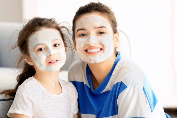 Young woman and her little daughter with facial masks at home - Фото, изображение