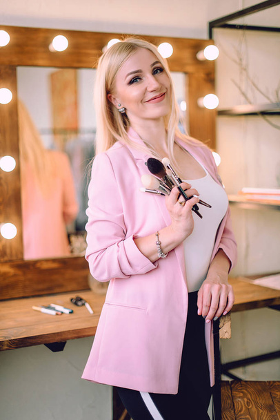 Make-up artist positive beautiful blonde woman posing near mirror in make-up room - Foto, afbeelding
