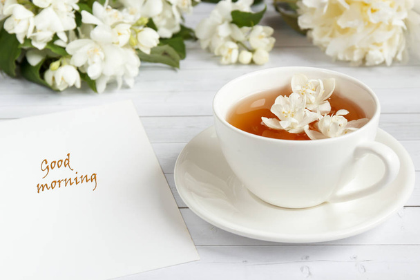 Cup of tea, pouring honey from a spoon in a jar, Jasmine flowers on a light wooden background. Copy space. - Photo, Image