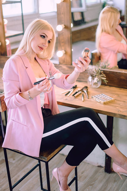 Portret van een mooie blonde vrouw toepassing van make-up in de buurt van een spiegel - Foto, afbeelding