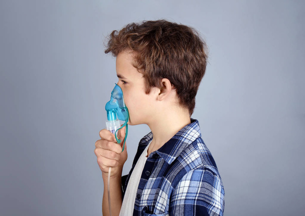 Young boy using nebulizer for asthma and respiratory diseases on light background - Foto, imagen