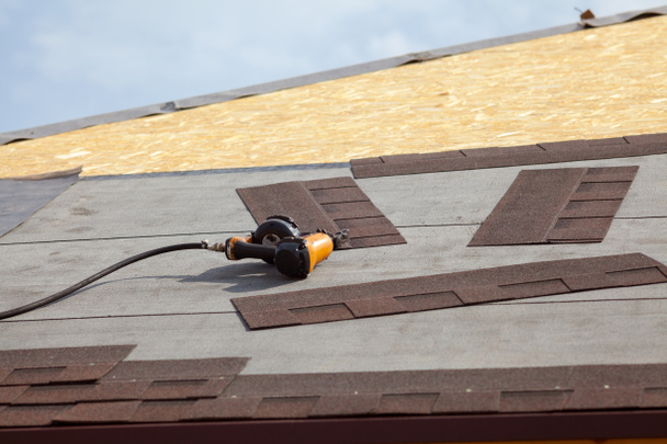 Pistola de clavos en una nueva casa marco con techo de asfalto nuevo (tejas
). - Foto, imagen