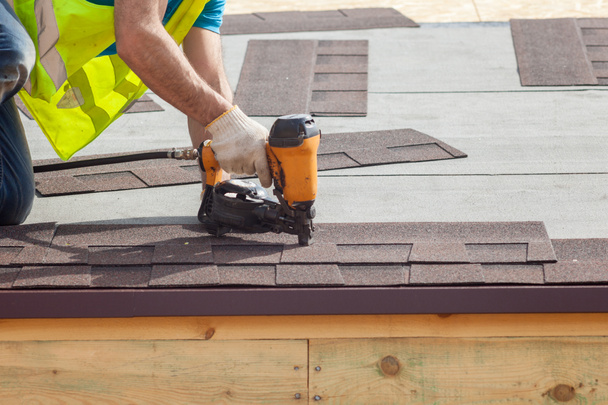 Rakennustyöntekijä laittaa asfaltti katto (vyöruusu) naulapyssy uuteen runko talo
. - Valokuva, kuva