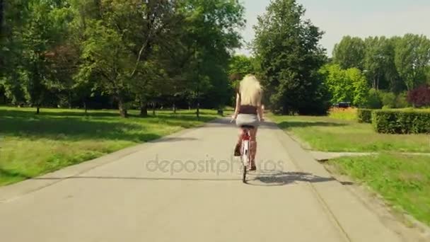 Unknown blonde woman cycling along park road - Felvétel, videó