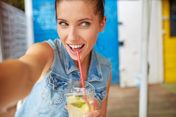 Lovely young smiling woman drinking lemonade and make a selfie. - Foto, Imagem