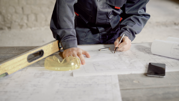 Közelkép a férfi kezét vonalakat tervei és specifikáció. Építési terv, szint, védő szemüvegek és smartphone hazudik a fából készült íróasztal projektben dokumentumokkal. - Felvétel, videó