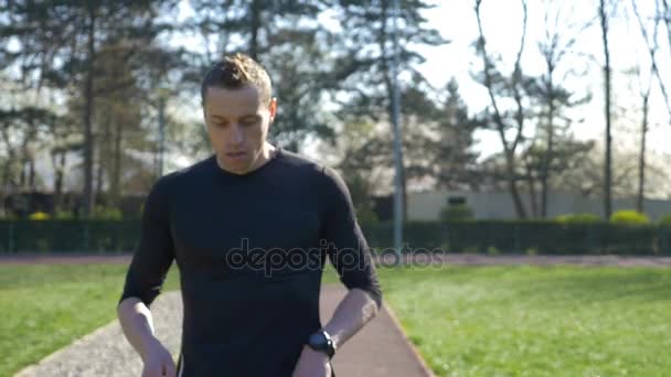 Closeup of tired young athlete in tracksuit stopping to rest after jogging in the park then starting to run - Filmati, video