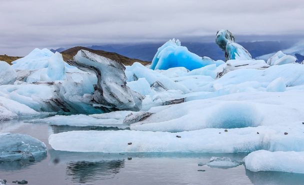 Lenyűgöző téli nap kilátás Jokulsarlon, jeges folyó lagoon, nagy gleccsertó, Délkelet-Izland, a szélén a Vatnajkull Nemzeti Park, Izland természeti csodája. Nagy világító kék jéghegy hasonlít kísérteties lovag lovas ló - Fotó, kép