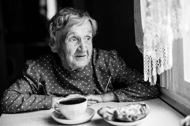 Vanha nainen istuu ikkunan vieressä
 - Valokuva, kuva