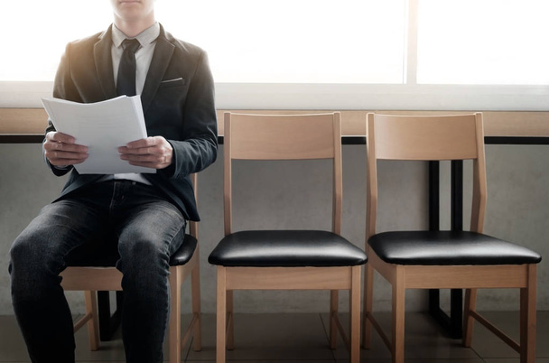 selbstbewusster junger Geschäftsmann, der Papier hält, während er auf einer Stuhlreihe sitzt - Foto, Bild
