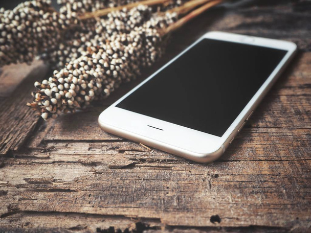 смартфон с чистым экраном и красивыми сушеными цветами на деревянном столе
 - Фото, изображение