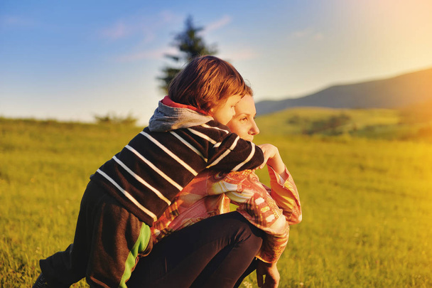 夏に山で草の上に座って幼児ハグする母 - 写真・画像