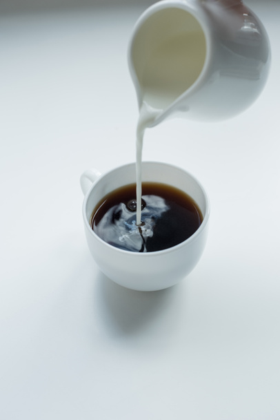 pouring milk into cup of black coffee  - Фото, зображення