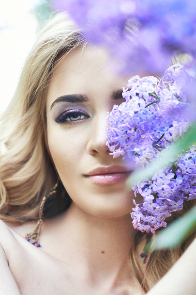 Outdoor fashion beautiful young woman surrounded by lilac flowers summer. Spring blossom lilac bush. Portrait of a girl blondes. - Fotoğraf, Görsel