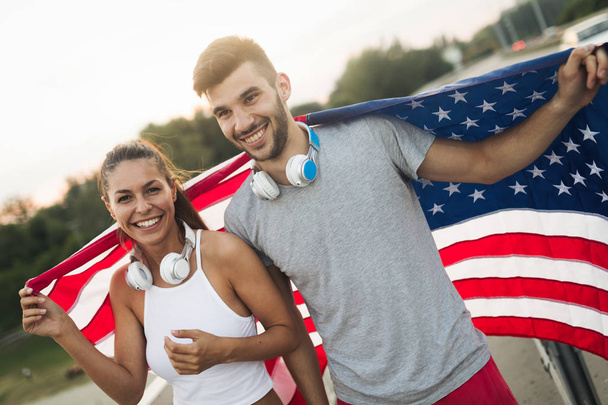 Portrait of attractive fitness couple holding American flag - Foto, imagen