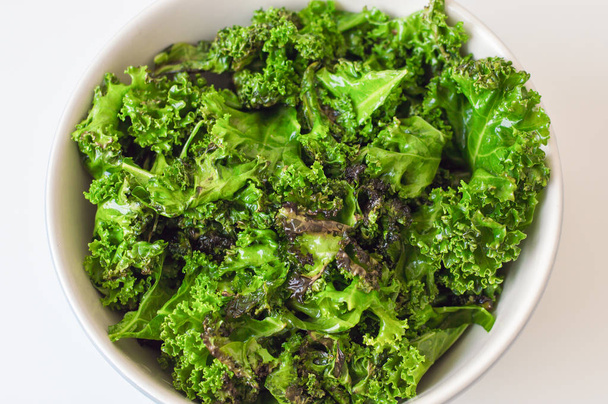 Kale salad in big bowl on white table. Fresh oily kale leaves. Healthy food - Photo, image