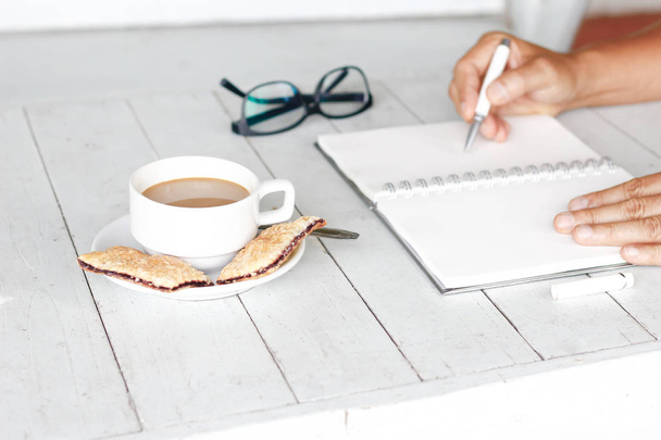 Stock photo Cropped image of a man sitting at vintage white wooden table and coffee while working with notepad - Photo, Image