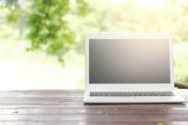 Zdjęcie stockowe komputer laptop z pusty ekran wstecz na drewnianym stole z tło zielony natura ogród - Zdjęcie, obraz