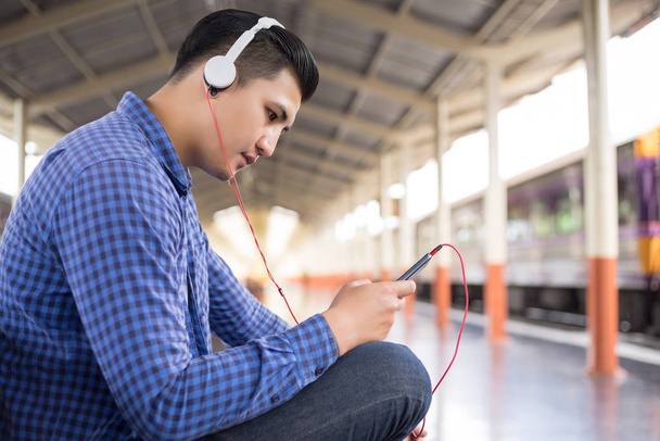 man traveler with backpacker listening to music at trainstation - Foto, Imagem