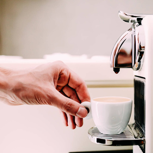 Close up of hand of barista brewing coffee using a coffee machine. The man is standing and holding a white cup - Foto, immagini