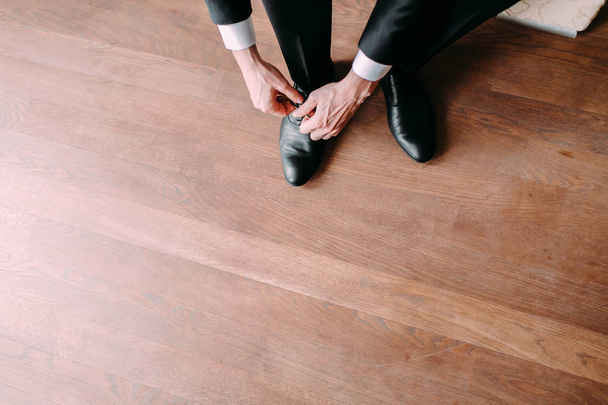 Liikemies sitomassa kengännauhoja lattialle. Sulhanen valmistautuu aamulla ennen häitä
 - Valokuva, kuva