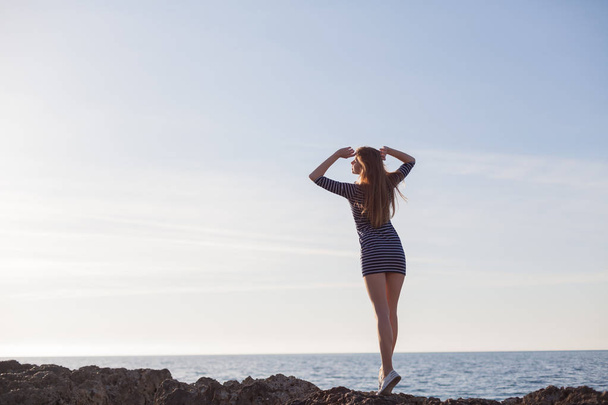 девушка на скальном пляже смотрит на море
 - Фото, изображение