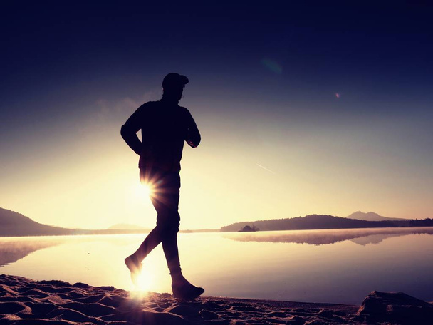Man running on beach against backdrop of a beautiful sunset. Sand of mountain lake - Photo, Image