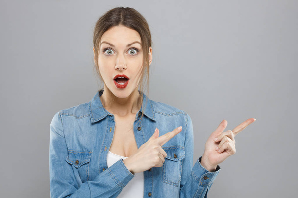 Closeup of good looking female isolated on gray background pointing with both hands to right side of picture with eyes and mouth open wide with surprise and astonishment about positive news. - Foto, Imagem