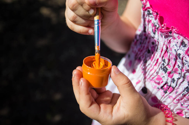 Een kind heeft een oranje verf en een borstel in zijn hand - Foto, afbeelding