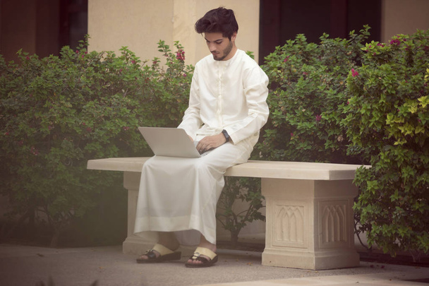 Emiraty młody mężczyzna pracujący z jego laptopa poza  - Zdjęcie, obraz