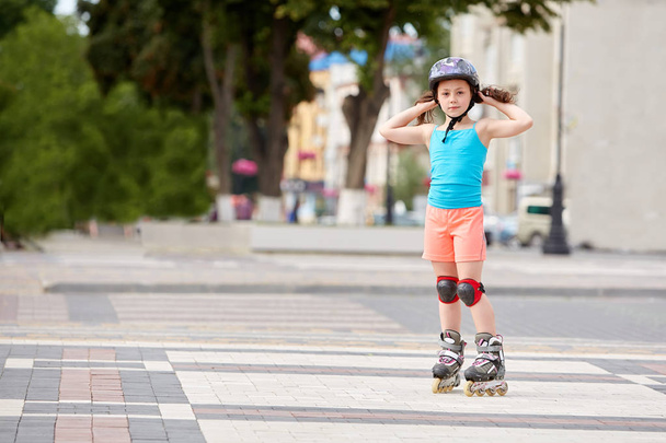 Funny Little pretty girl on roller skates in helmet riding in a park. - Foto, Imagen