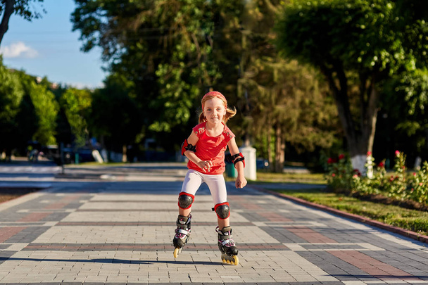Girl riding on roller skates in skatepark summer outdoor. Child in a red suit for the rollers - Foto, Imagem