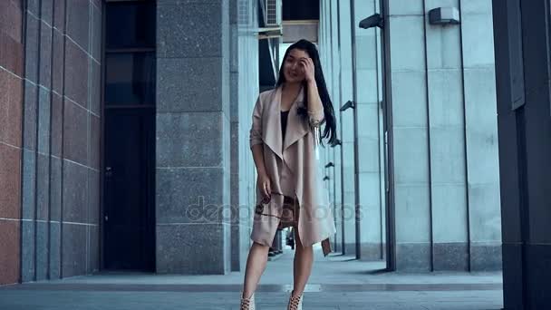 Милая и красивая азиатка в пальто ходит среди колонн
 - Кадры, видео