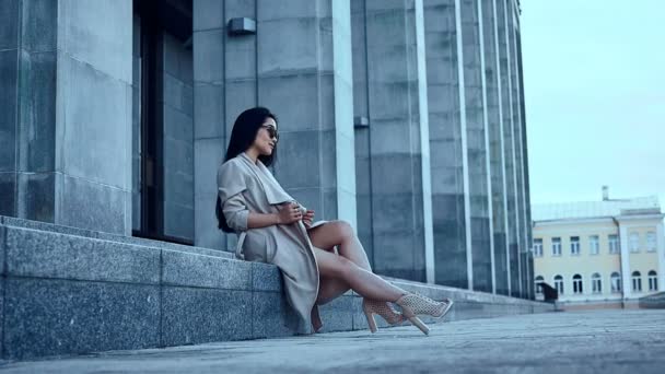 Linda y hermosa mujer asiática en abrigo sentado en los pasos
 - Metraje, vídeo
