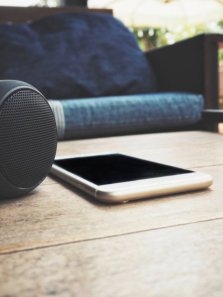 smartphone and bluetooth speaker lying on table at home with sofa on background - Photo, Image