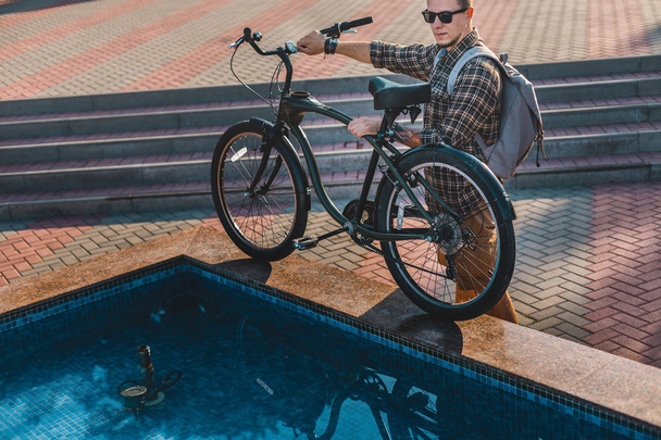 Jonge wielrenner zet zijn fiets aan rand van stad fontein dagelijkse levensstijl stedelijke rusten Concept - Foto, afbeelding