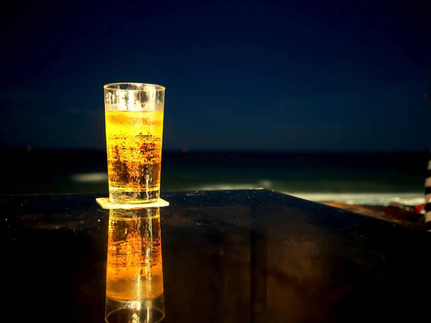Pohár sör az asztalon, a strandon, éjszaka folyamán. - Fotó, kép