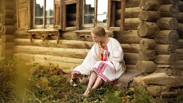Russische vrouw met een kat in de buurt van oude houten huis in een dorp - Foto, afbeelding