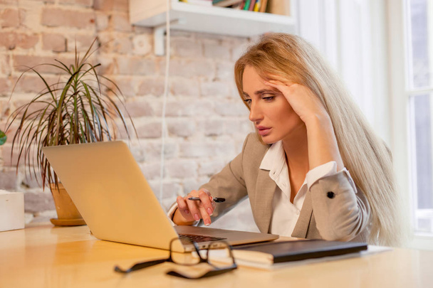 Μακρυμάλλης ξανθός που εργάζονται με το laptop της σε ένα ωραίο γραφείο. Γυναίκα που φοράει ρούχα bussunes. - Φωτογραφία, εικόνα