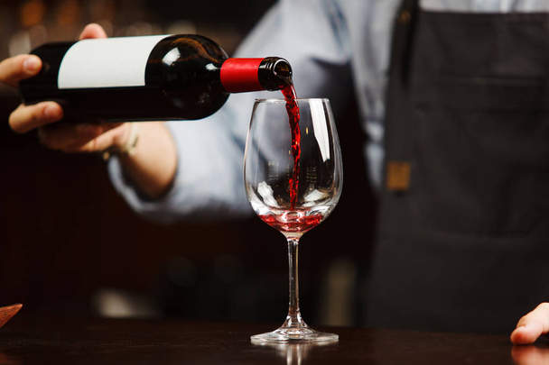 Waiter pouring red wine into wineglass. Sommelier pours alcoholic drink - 写真・画像