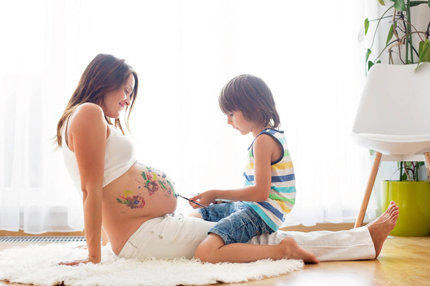 Boldog gyermek, fiú, Mami terhes hasa festés - Fotó, kép