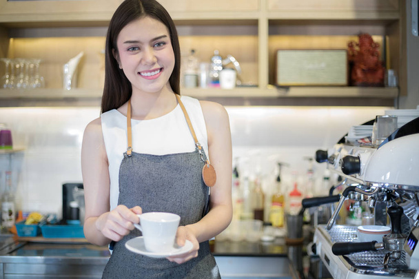 Mujeres asiáticas Barista sonriendo y sosteniendo la taza de café y usando mac
 - Foto, imagen