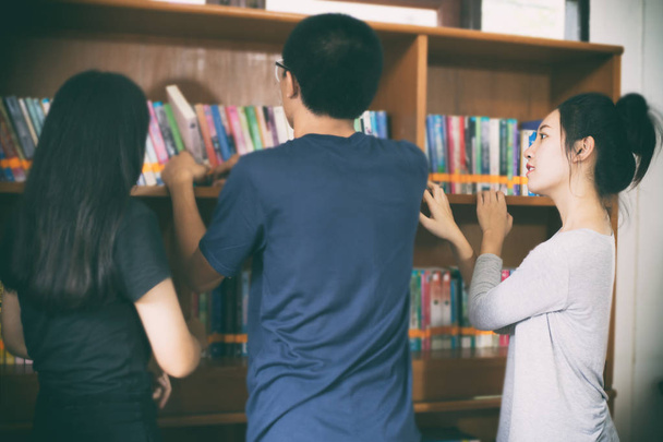 Asiática mujer estudiantes holding para selección libro en biblioteca
 - Foto, imagen