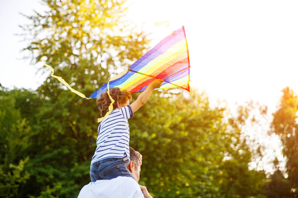 Boy sitting on father shoulders holding kite - 写真・画像
