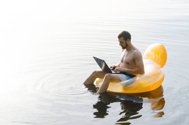 Чоловік з ноутбуком на надувному кільці у воді на заході сонця
 - Фото, зображення