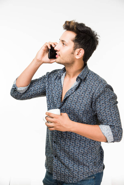 白い背景に分離立ってコーヒーのカップを持つ若いハンサムなインド男性の肖像画 - 写真・画像