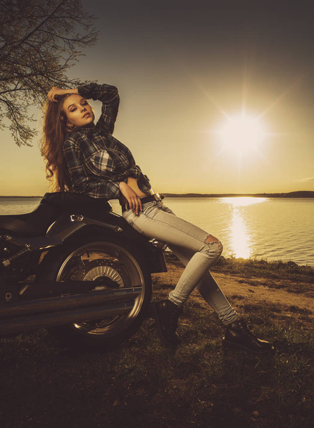 Молода дівчина біля мотоцикла на озері. Захід сонця
. - Фото, зображення