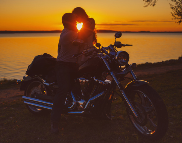 Dois amantes com moto ao pôr do sol na margem do lago
 - Foto, Imagem